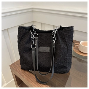 Détail du sac cabas en toile noire texturée avec bandoulière chaîne sur table