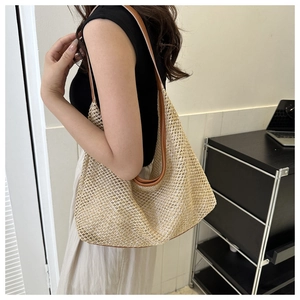 Detail of a large woven tote bag in cream with brown leather straps worn by a model