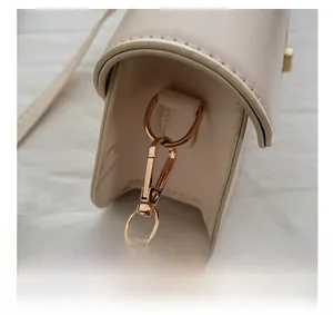 Gros plan sur les anneaux en D dorés et les mousquetons du sac en cuir crème