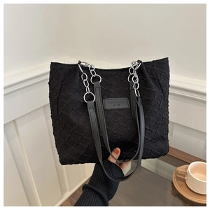 Détail d'un sac cabas noir texturé avec chaîne en métal argenté et étiquette mode