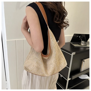 Detail of a large woven hobo bag with brown leather shoulder straps and beige texture