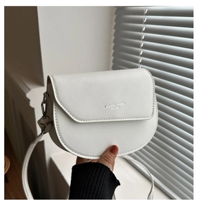 Détail du sac selle blanc semi-circulaire montrant le logo argenté et les ferrures