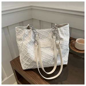 Détail du cabas blanc à texture tissée avec chaîne en métal et écusson en cuir
