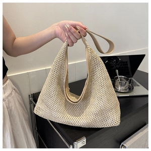 Detail of beige hollow-out woven straw tote bag with brown leather shoulder straps