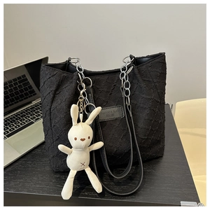 Détail du sac cabas noir avec bandoulière chaîne, écusson et breloque lapin