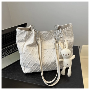 Gros plan du sac cabas en toile matelassée beige avec chaîne et breloque lapin doux