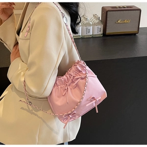 Détail du sac seau rose à cordon avec nœud et bandoulière chaîne sur modèle