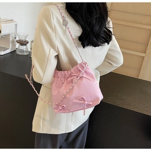 Detail of pink drawstring bucket bag featuring soft ribbon bows and chain strap