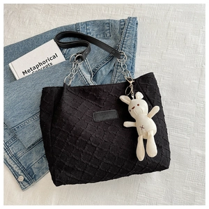 Détail d'un sac cabas noir gaufré avec bandoulière en chaîne et pendentif lapin