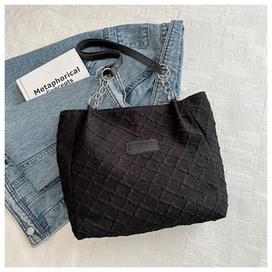 Détail du sac cabas en toile noire texturée avec bandoulière chaîne et patch en cuir