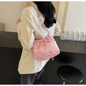 Détail du sac seau plissé rose avec nœuds et bandoulière en chaîne sur un mannequin