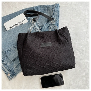 Détail du sac cabas en toile noire texturée avec chaînes et écusson de marque