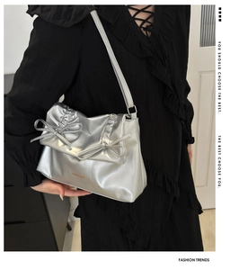 Detail of silver metallic tote bag with bow accents worn by a model in a black dress