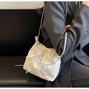 Détail du sac plissé blanc avec nœud décoratif et bandoulière chaîne sur l'épaule