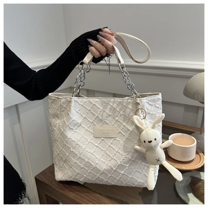 Détail d'un sac cabas en toile crème avec texture tissée, chaîne en métal et breloque lapin