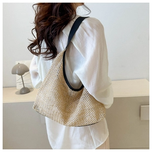 Detail view of woven straw hobo bag with black trim on a model's shoulder for casual style