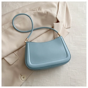 Detail of light blue leather handbag with circular handle and gold buckle on beige fabric