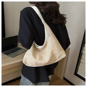 Detailed side view of large beige woven straw tote bag worn by a model in black blazer