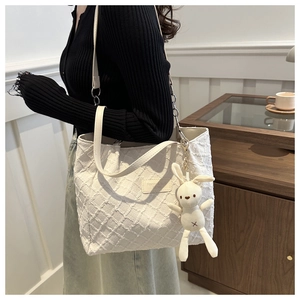 Détail du cabas en toile tissée blanc cassé avec bandoulière en cuir et pendentif lapin