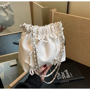 Détail du sac à main plissé crème avec nœuds décoratifs et bandoulière chaîne