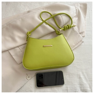 Détail d'un sac bandoulière vert fluo avec bandoulière nouée et plaque dorée avec mobile