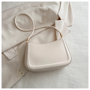Detail of a creamy white crescent shoulder bag with gold hardware on a beige suit fabric