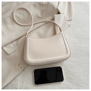 Detail view of cream shoulder bag with phone for scale on white textured fabric