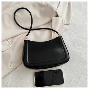 Close-up of minimalist black leather underarm bag with gold hardware next to a smartphone