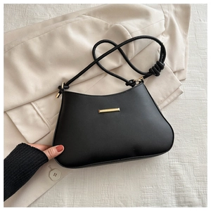 Détail du sac sous l'aisselle en cuir noir minimaliste avec accastillage doré et bandoulière nouée