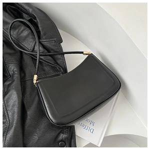 Close-up of minimalist black leather shoulder bag with sleek golden metal buckle detail