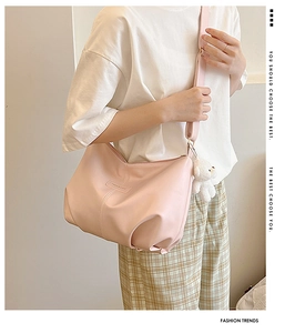 Side view of pink PU leather tote bag with wide strap and plush bear charm on a model