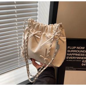 Détail d'un sac seau plissé beige avec des nœuds décoratifs et une bandoulière chaîne