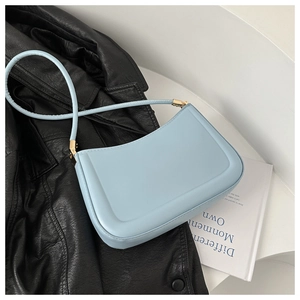 Detail view of light blue shoulder bag with gold hardware on a leather background