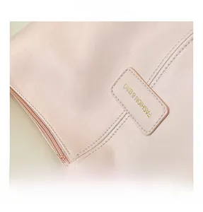 Detailed close-up of light pink pebble leather bag with gold embossed logo text