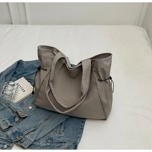 Detail view of a taupe tote bag with drawstring accents and long shoulder straps