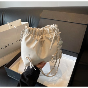 Détail du sac seau plissé crème avec nœuds et bandoulière en chaîne dans un coffret cadeau
