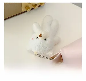 Close-up of a soft white plush rabbit charm with a silver bead chain on a pink leather bag