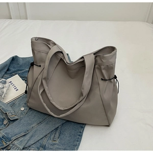 Detail of high-capacity grey nylon tote bag with drawstring closure on white bedding