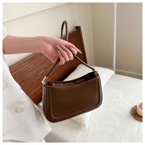 Detail of dark brown leather underarm bag with gold metal hardware and rounded bottom