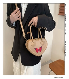 Detail of khaki heart-shaped handbag featuring red butterfly embroidery and shoulder strap