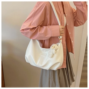 Detail of white crescent tote bag with plush bear pendant and fashion text label