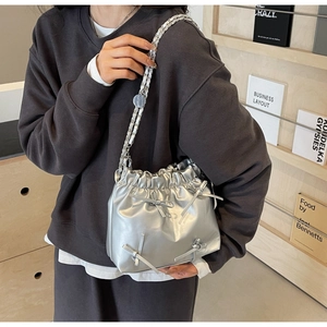 Detail of silver metallic pleated bucket bag with bows and chain strap worn by a model
