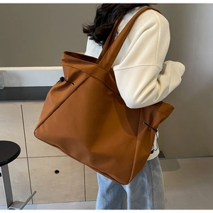 Detail of a brown tote bag with side drawstring and high-density material on a model