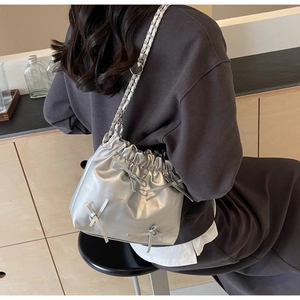 Détail du sac seau métallisé argenté avec des nœuds décoratifs et bandoulière chaîne