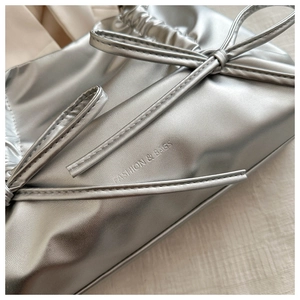Close-up of metallic silver bow detail and embossed fashion logo on the pleated tote bag