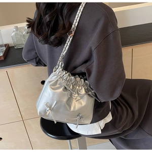 Close-up of silver pleated bucket bag with bows and metallic chain strap detail