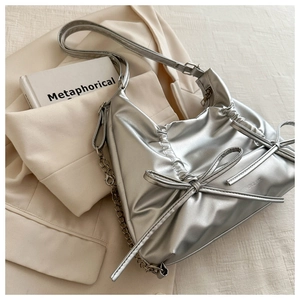 Detail of silver pleated tote bag with bows on a blazer next to a lifestyle magazine