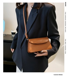 Brown retro baguette bag in glossy leather texture worn crossbody by a model in a suit
