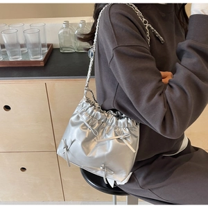 Détail d'un sac seau métallisé argenté avec nœuds délicats et bandoulière en chaîne