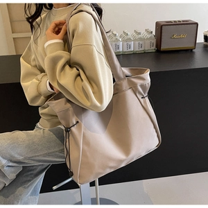 Detail of a large beige tote bag with functional side drawstring and smooth texture